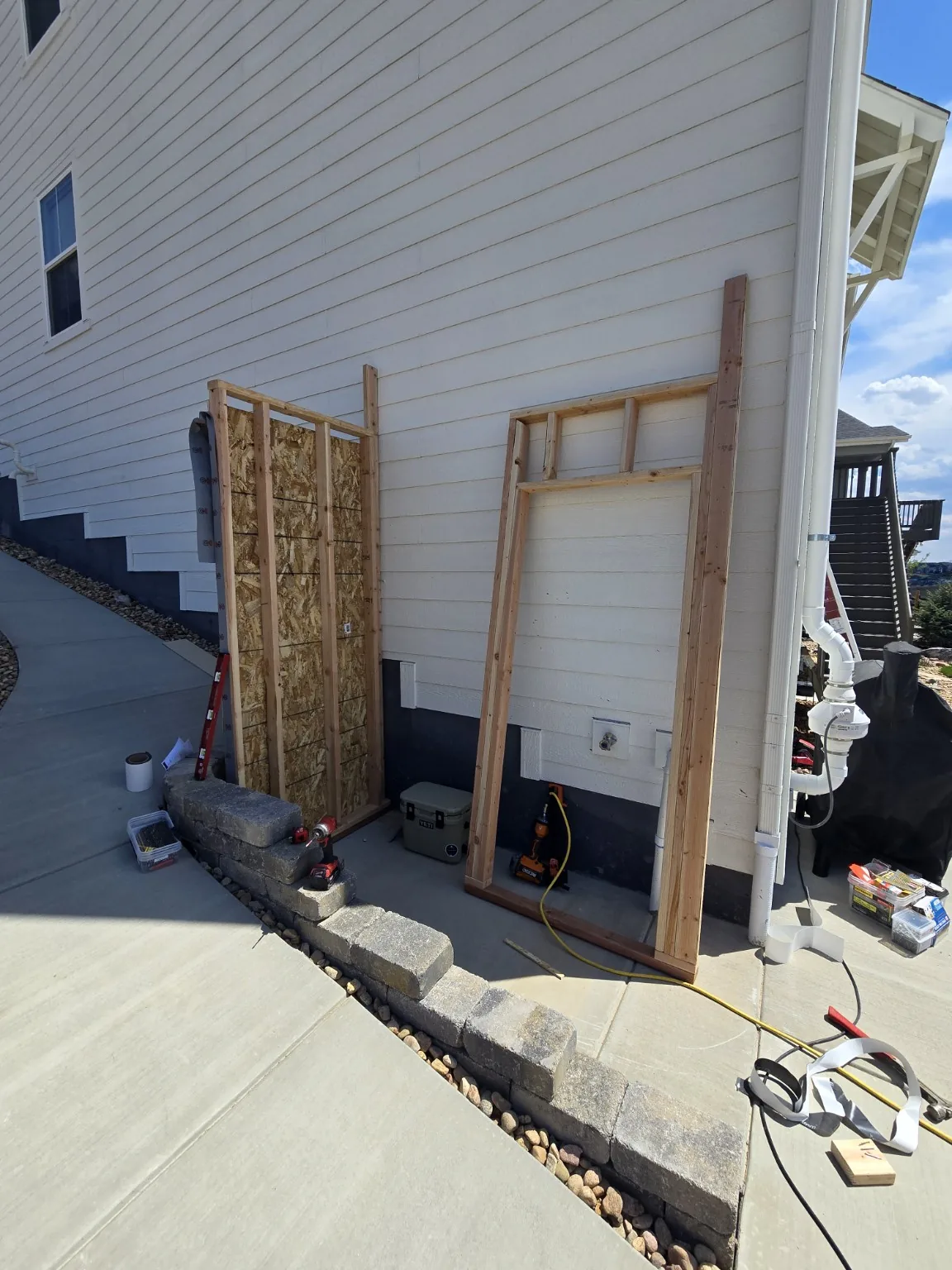 Framed and sheathed wall sections staged against the house before the Castle Rock basement entrance enclosure was set