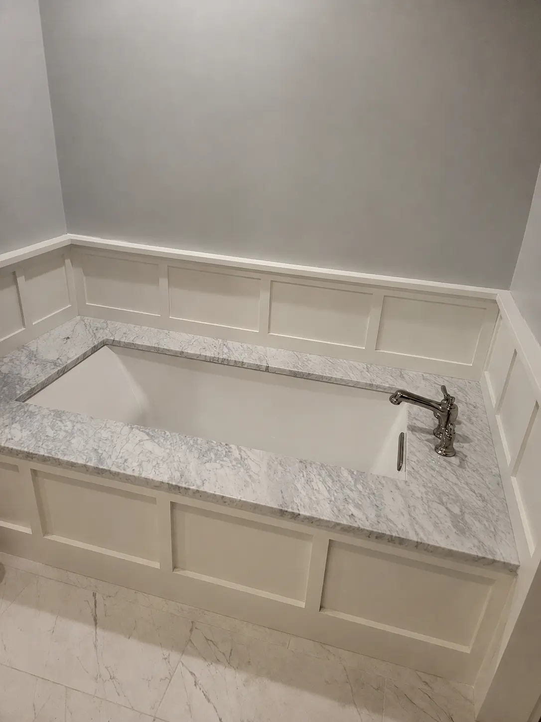 Completed bathtub with marble-look surround and white paneled walls