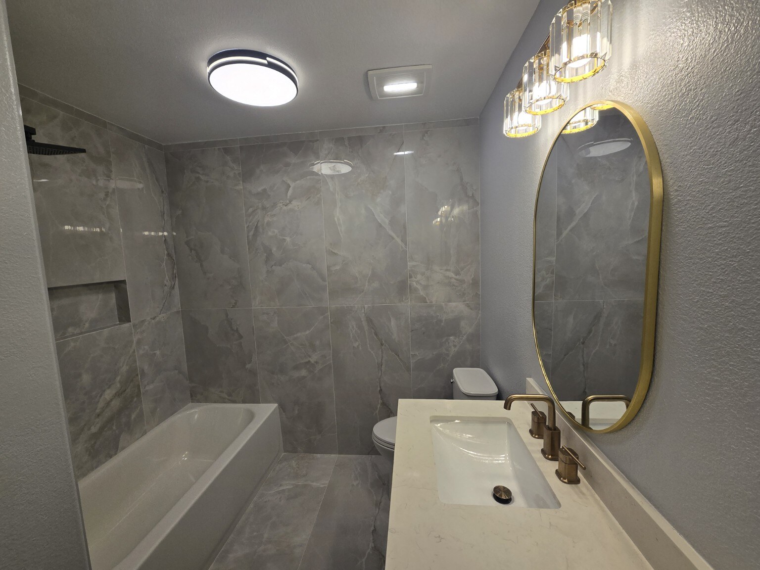 Renovated Littleton bathroom with new bathtub, polished gray tile walls and gold-tone mirror
