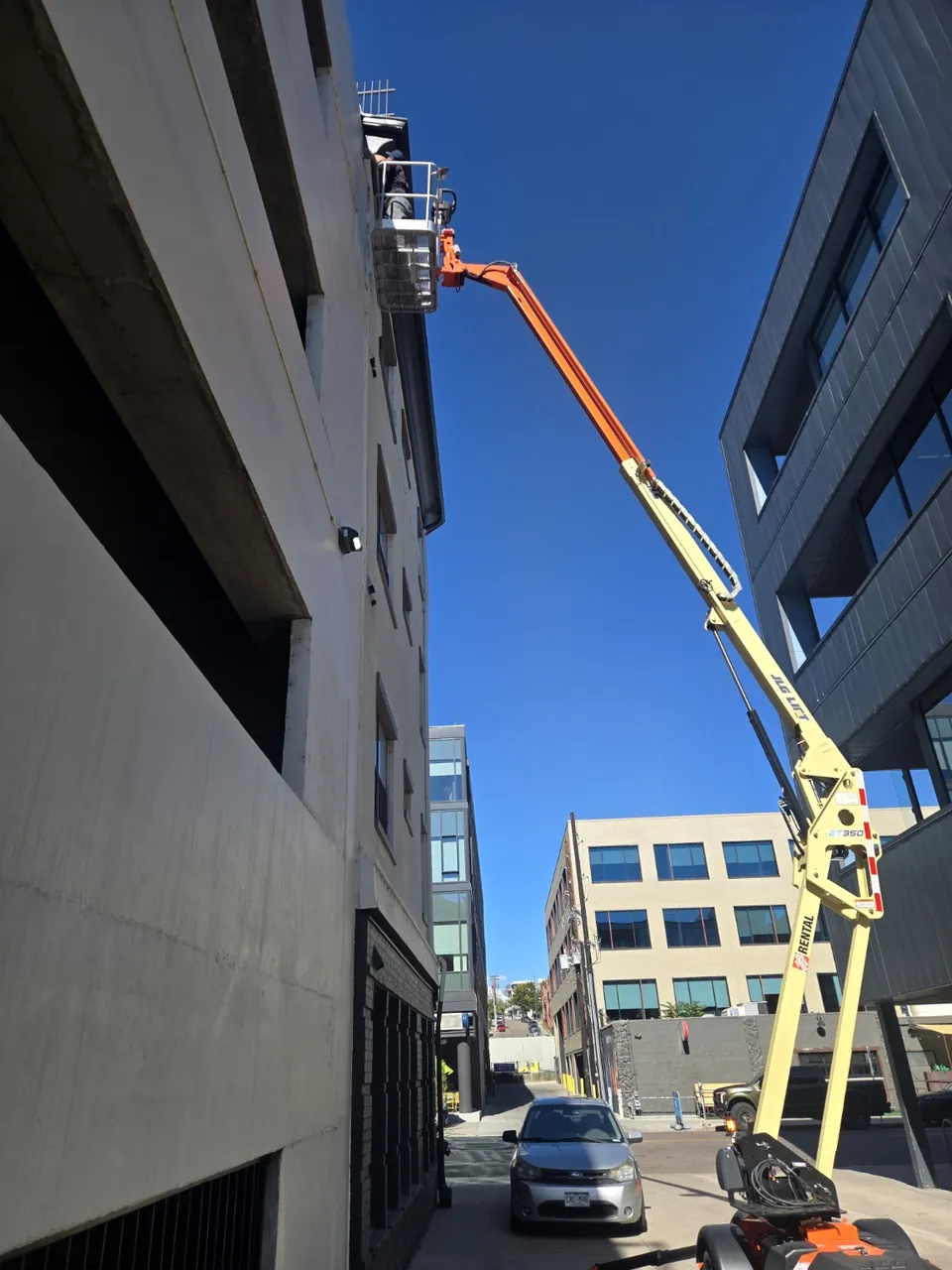 Worker in a raised aerial work platform basket at the roofline of a multi-story building