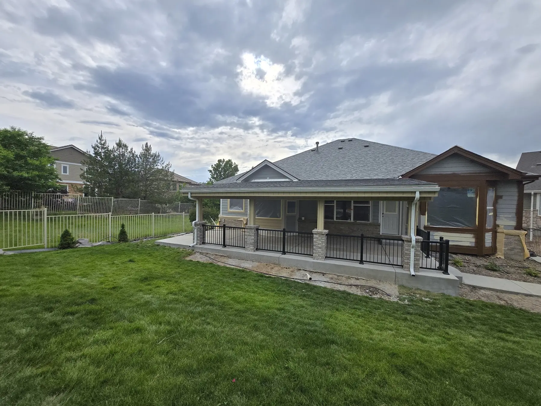 Completed covered patio with masonry columns and black aluminum railings at an Aurora home