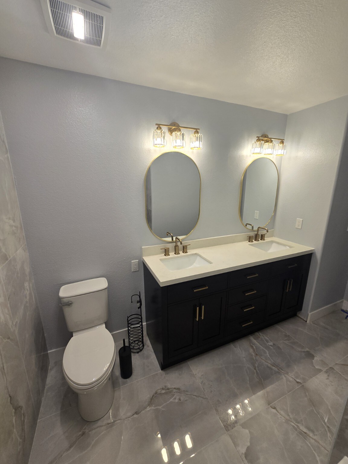 Finished Littleton bathroom with black double vanity, two oval gold mirrors and polished gray floor tile