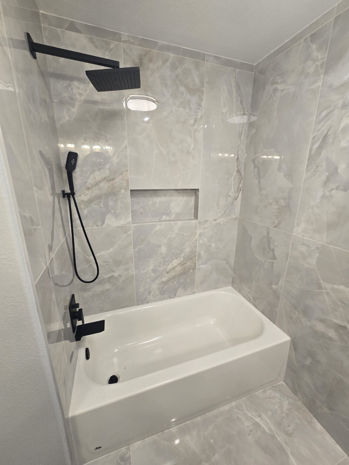 New bathtub and shower with recessed niche, gray stone-look tile and matte-black rainfall fixtures