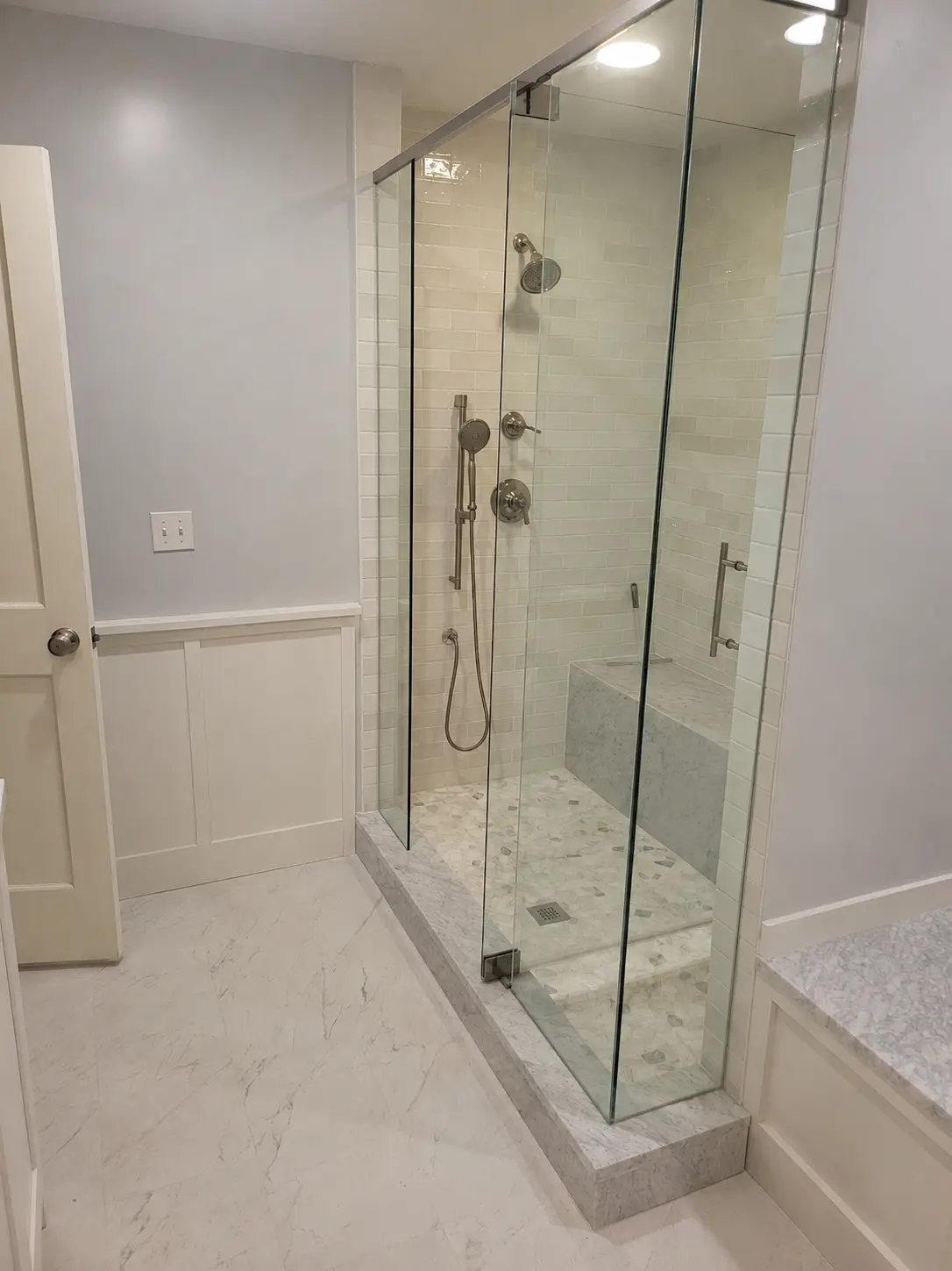 Completed walk-in shower with glass enclosure, tiled walls, bench and handheld shower
