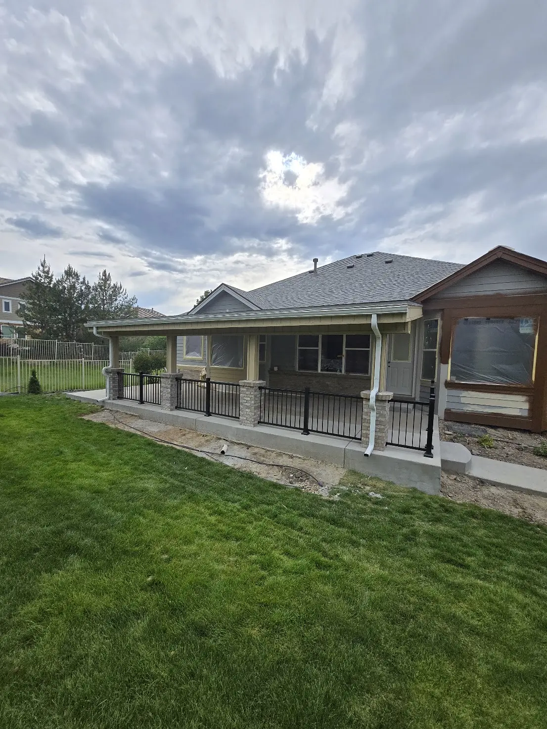 Wide perspective of a finished asphalt-shingle patio cover with gutters and aluminum railings in Aurora