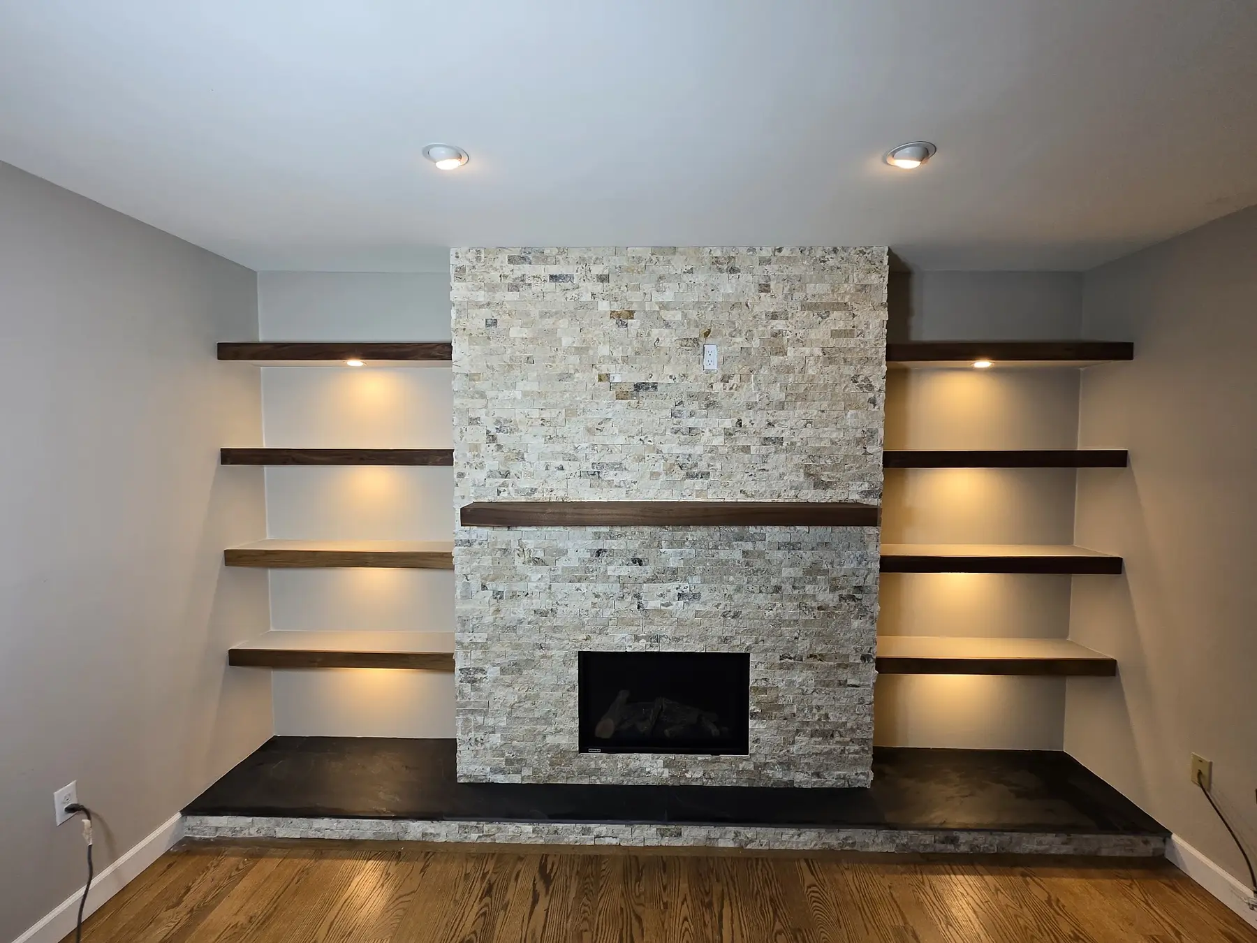 Completed gas fireplace with manufactured-stone surround, wood mantel, built-in shelves and accent lighting in Centennial