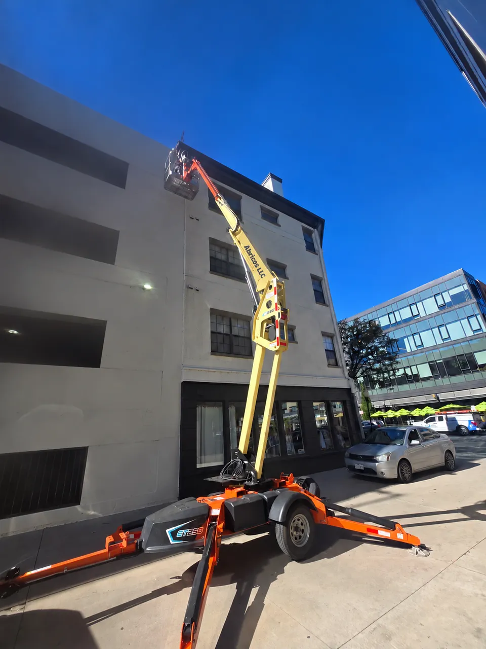 Aerial work platform raised to the roofline of a multi-story stucco building for exterior repairs